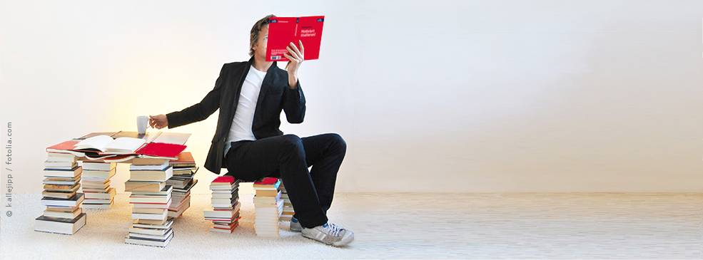 Mann sitzt auf Bücherstapeln und liest ein utb-Buch